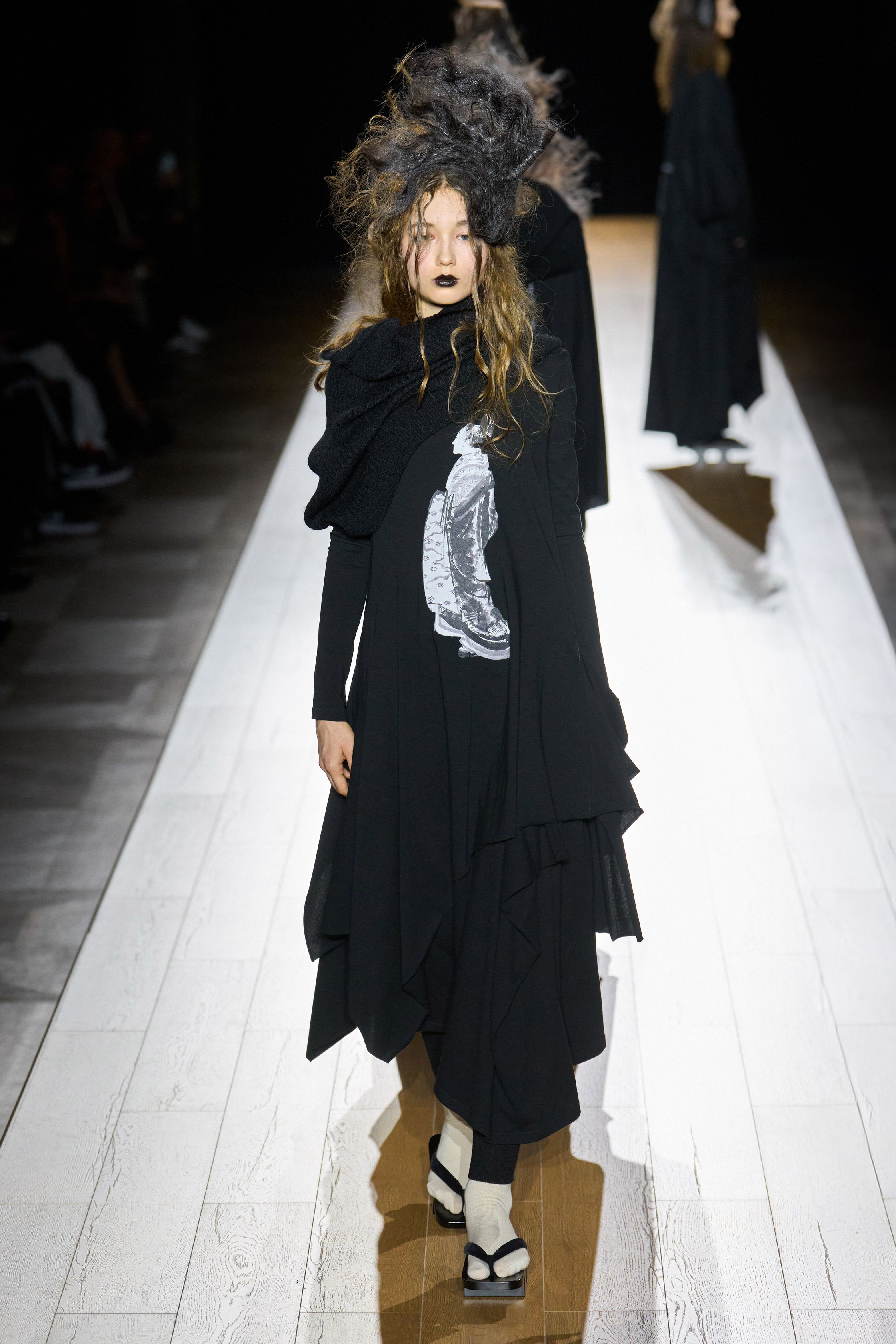 Yohji Yamamoto 本季依然延续标志性的黑色哲学：宽松层叠轮廓、和服式结构与手工拼接面料形成一种诗意而深沉的东方美学。夸张头饰与飘逸衣摆让整场秀像一场黑色戏剧，既神秘又极具艺术感-顽石频道趋势研究
